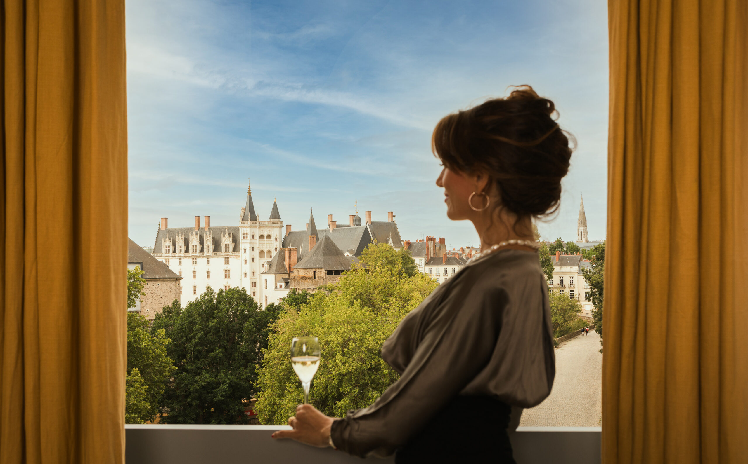 Femme avec une coupe de champagne à la fenêtre de sa chambre de Lhôtel Nantes avec vue sur le château